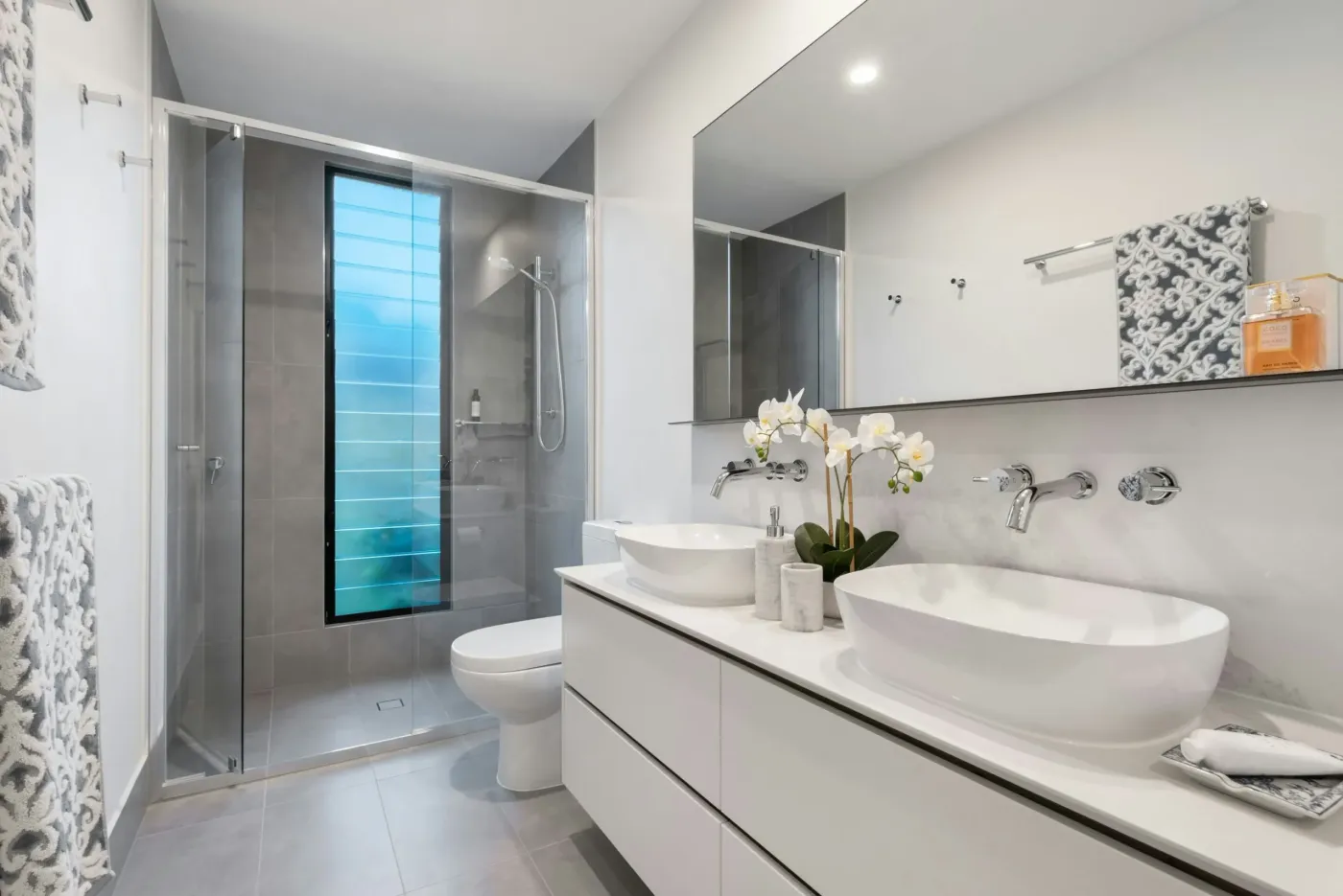 Modern bathroom with a glass-screened shower, twin vessel basins on a white floating vanity and a wide wall mirror