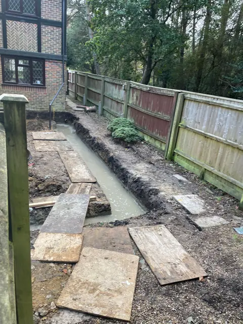 Fresh concrete in the foundation trench along the side boundary, with boards laid across the site