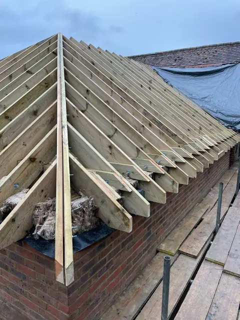Rafters meeting the hip at the corner of the new roof, above the brick wall