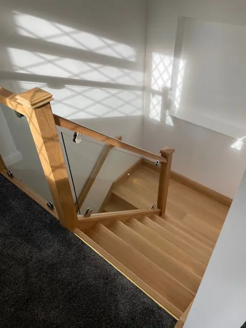 An oak staircase with a glass balustrade, seen from the landing