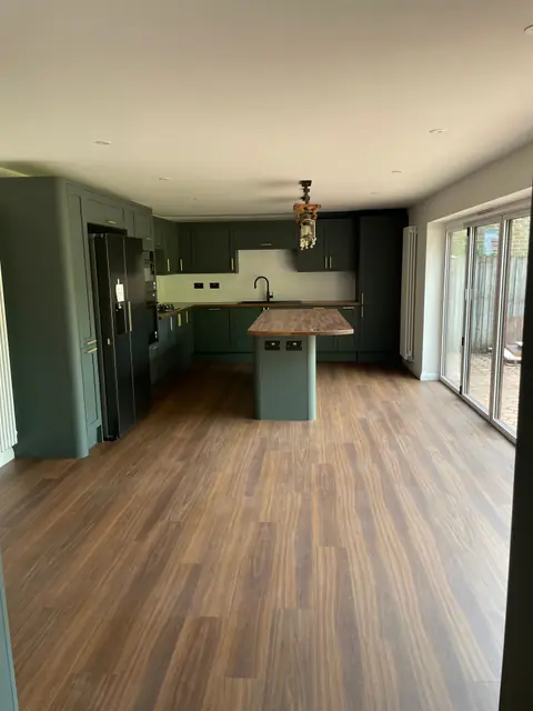The open plan kitchen, with green shaker units, an island and wood effect flooring, and bi-fold doors along one side