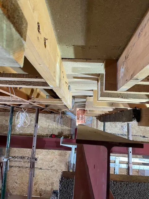 Looking up at a steel beam carrying the floor joists above, with temporary props below