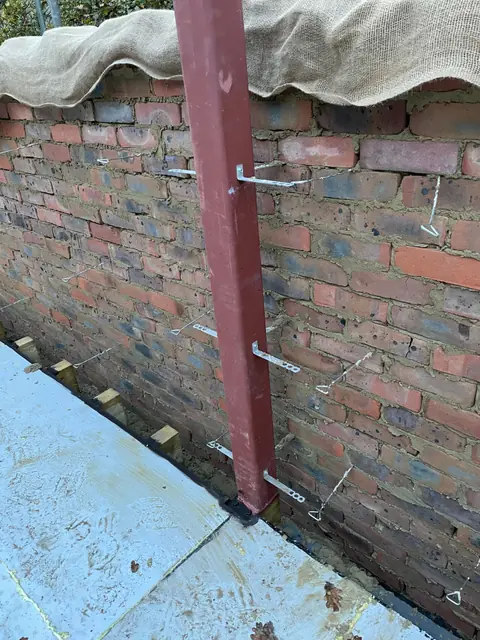 A steel post fixed against the existing brick wall, with wall ties ready for the new blockwork