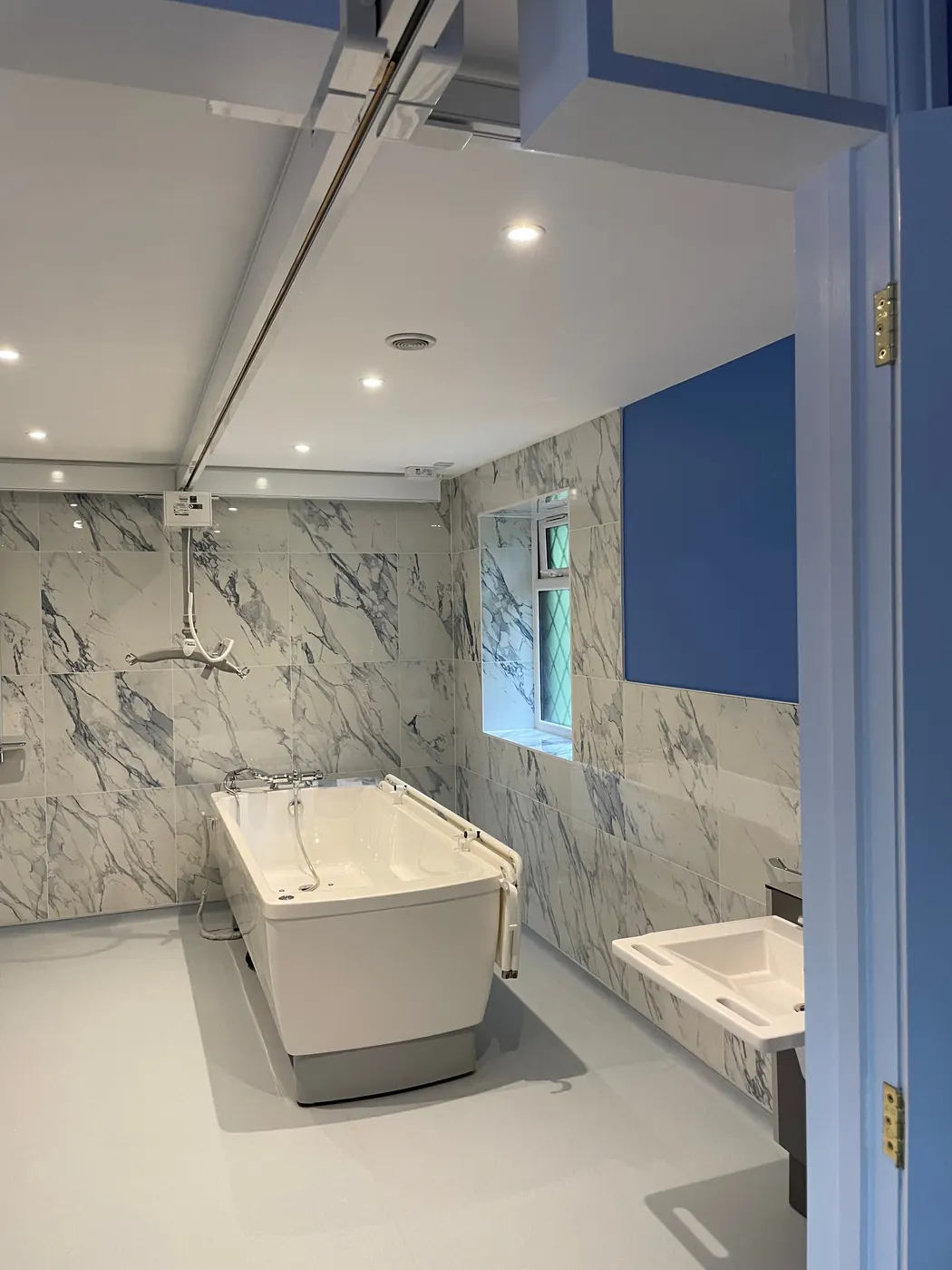 The finished wet room, with a ceiling hoist track above a height adjustable bath and marble effect wall panels