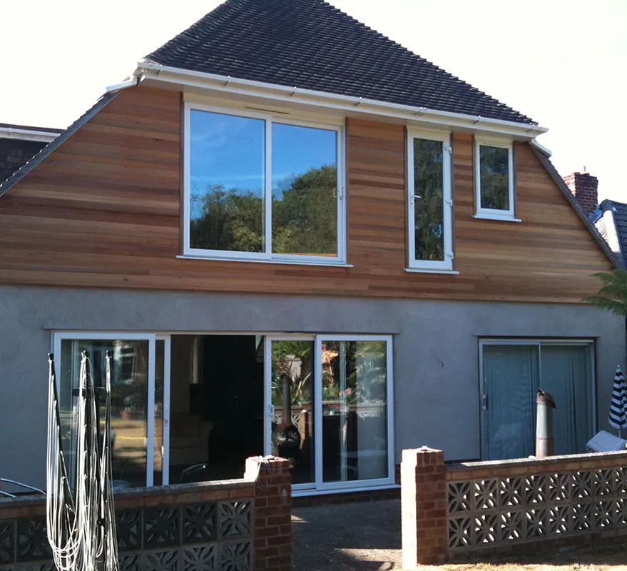 Rear of a house with a new first-floor extension clad in cedar, above white sliding patio doors