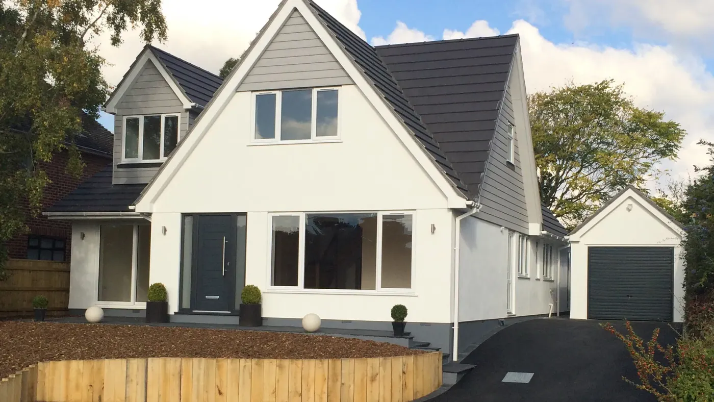 Remodelled chalet bungalow with white render, grey-clad gables and dormer, an anthracite front door and a new tarmac drive