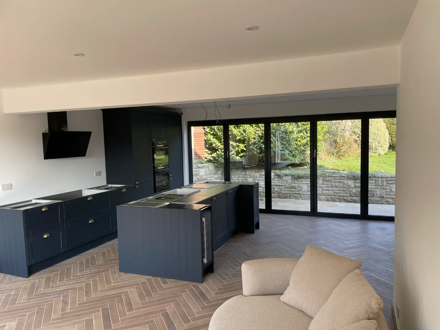 Open-plan kitchen extension with navy shaker units, an island, herringbone floor and bi-fold doors to the garden