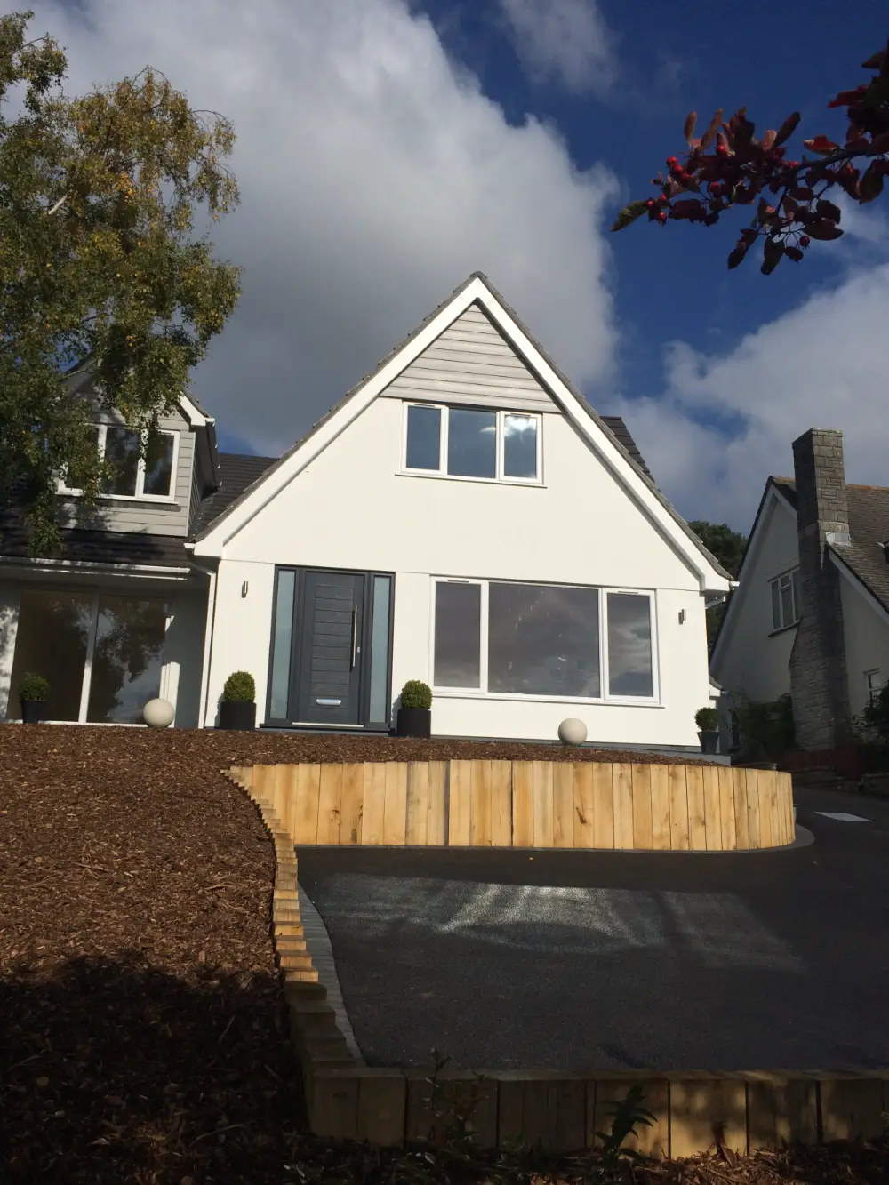 Finished chalet-style home with white render, grey cladding, an oak sleeper retaining wall and new driveway