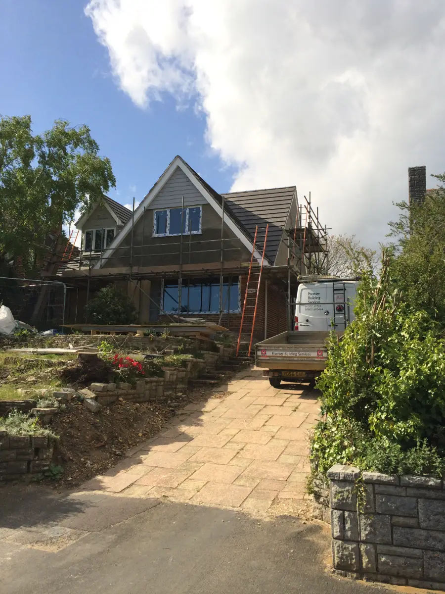 Front of a Bournemouth house mid-build, scaffolded with new gable framing and the Premier Building Services van on the drive