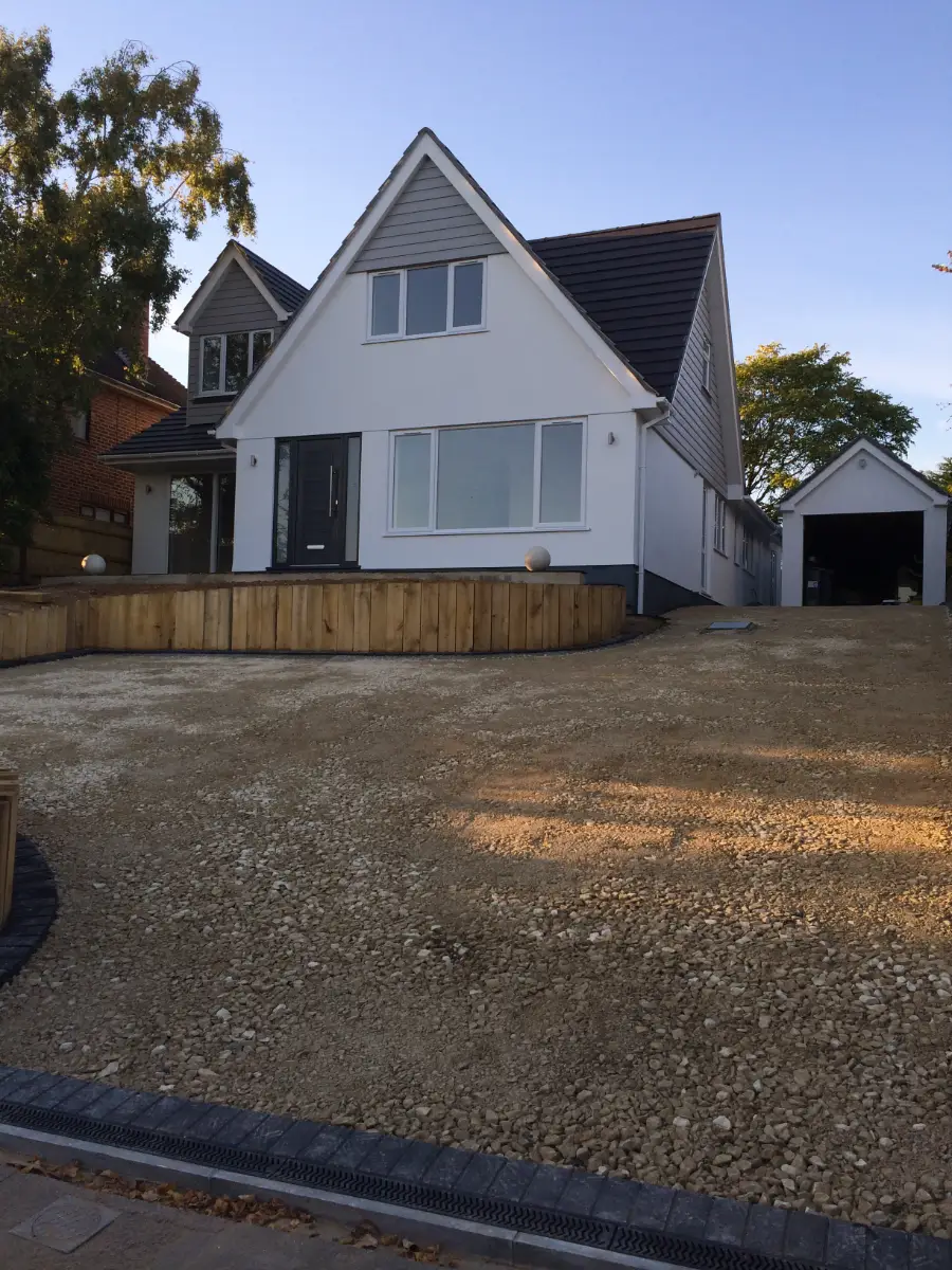 The same house completed, with a white rendered front elevation, grey cladding to the new gable and a resurfaced driveway