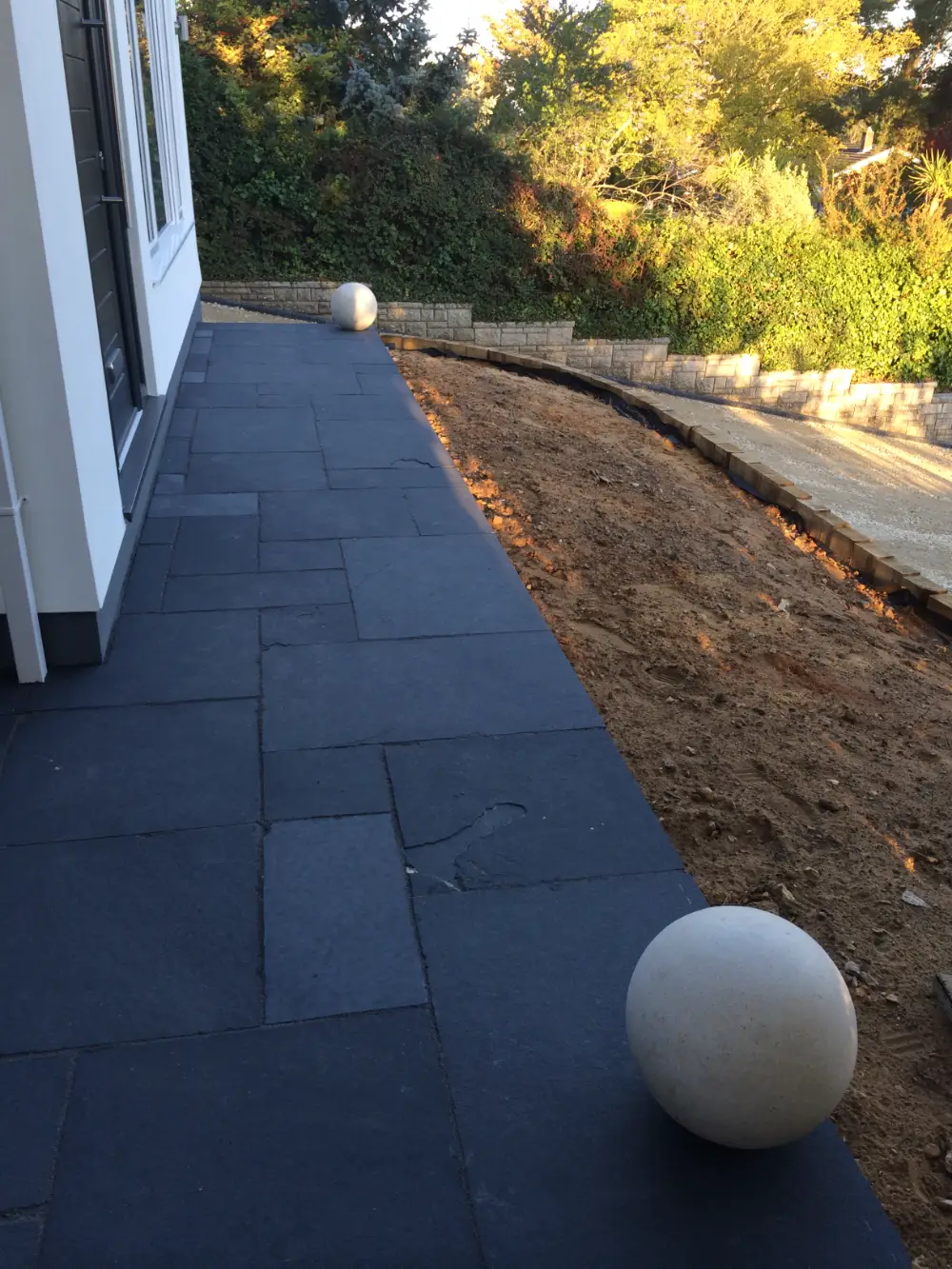 New slate patio running along a freshly rendered house, with stone spheres and new landscaping beyond