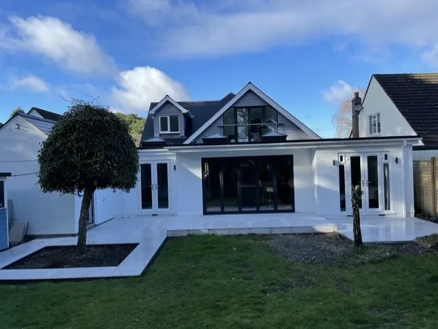 Rear of the finished house in Talbot Woods, with black aluminium bi-fold doors and two sets of French doors opening onto a pale stone patio, below a new glazed gable and dormer